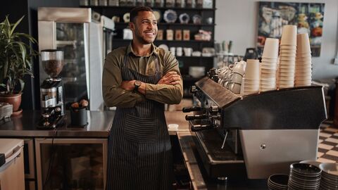Franchise Ein lachender Mann mit verschränkten Armen steht hinter dem Thresen seines Cafes